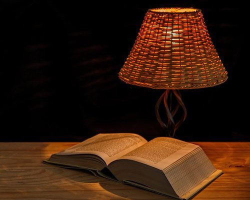 Soft light lamp standing on a wooden table next to an open paper book in a warm room layout